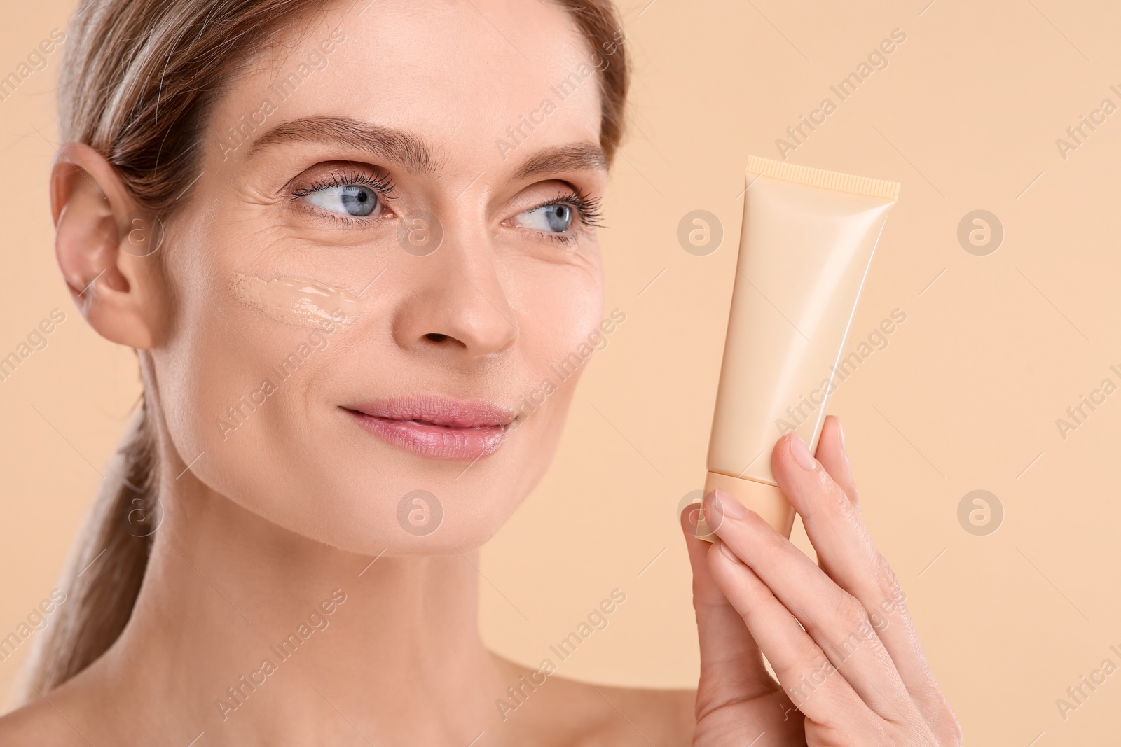 Photo of Woman holding tube of foundation on beige background