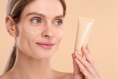 Woman holding tube of foundation on beige background