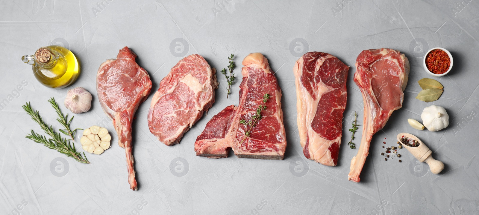 Photo of Fresh raw beef cuts, spices and oil on light grey textured table, flat lay