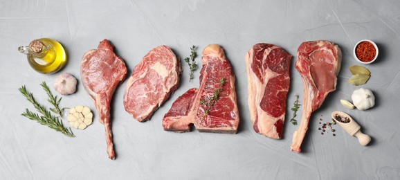 Fresh raw beef cuts, spices and oil on light grey textured table, flat lay