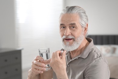 Photo of Senior man with glass of water taking pill at home