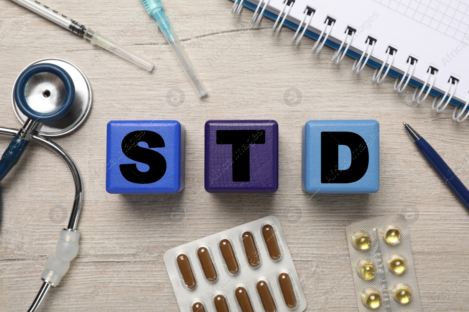 Photo of Flat lay composition with abbreviation STD, pills and stethoscope on wooden table