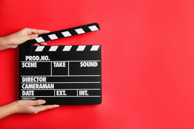 Photo of Woman holding clapperboard on red background, closeup with space for text. Cinema production