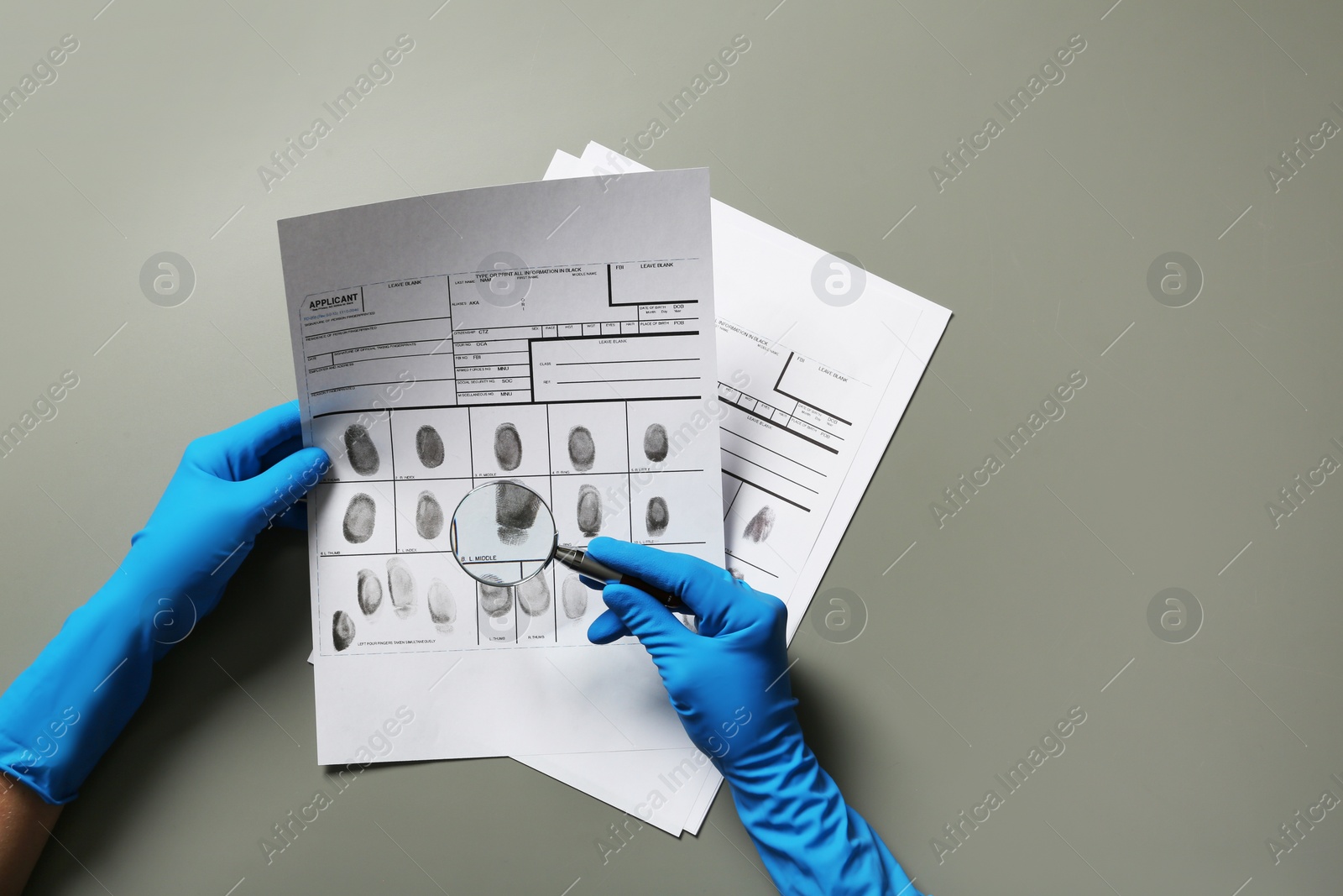 Photo of Criminologist exploring fingerprints with magnifier on grey background