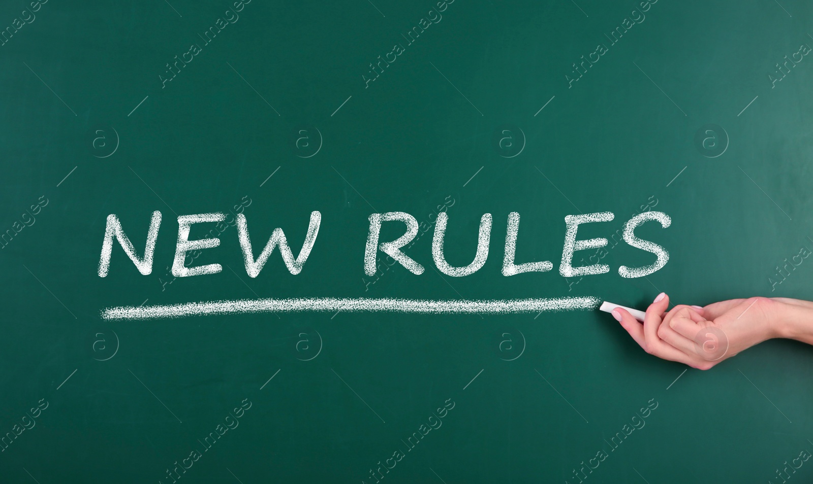 Image of Woman writing text NEW RULES on chalkboard, closeup