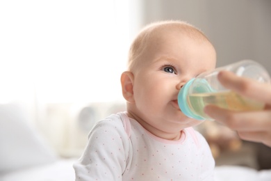 Lovely mother giving her baby drink from bottle in room