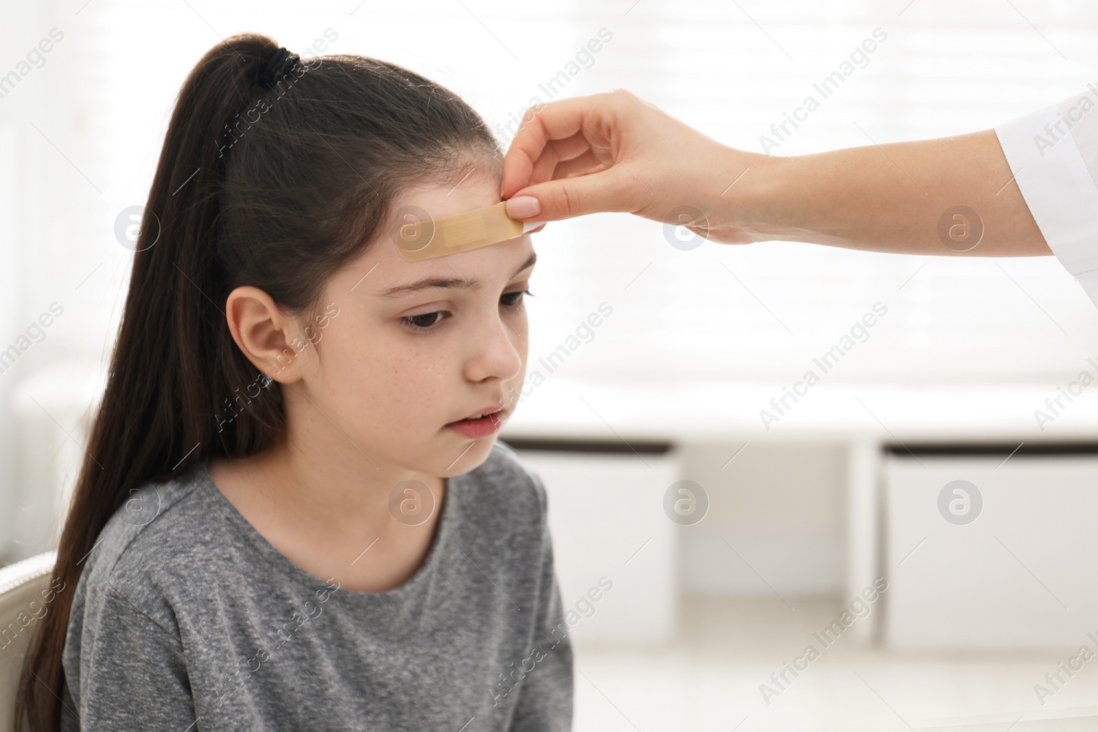 Photo of Doctor putting sticking plaster onto girl's forehead indoors