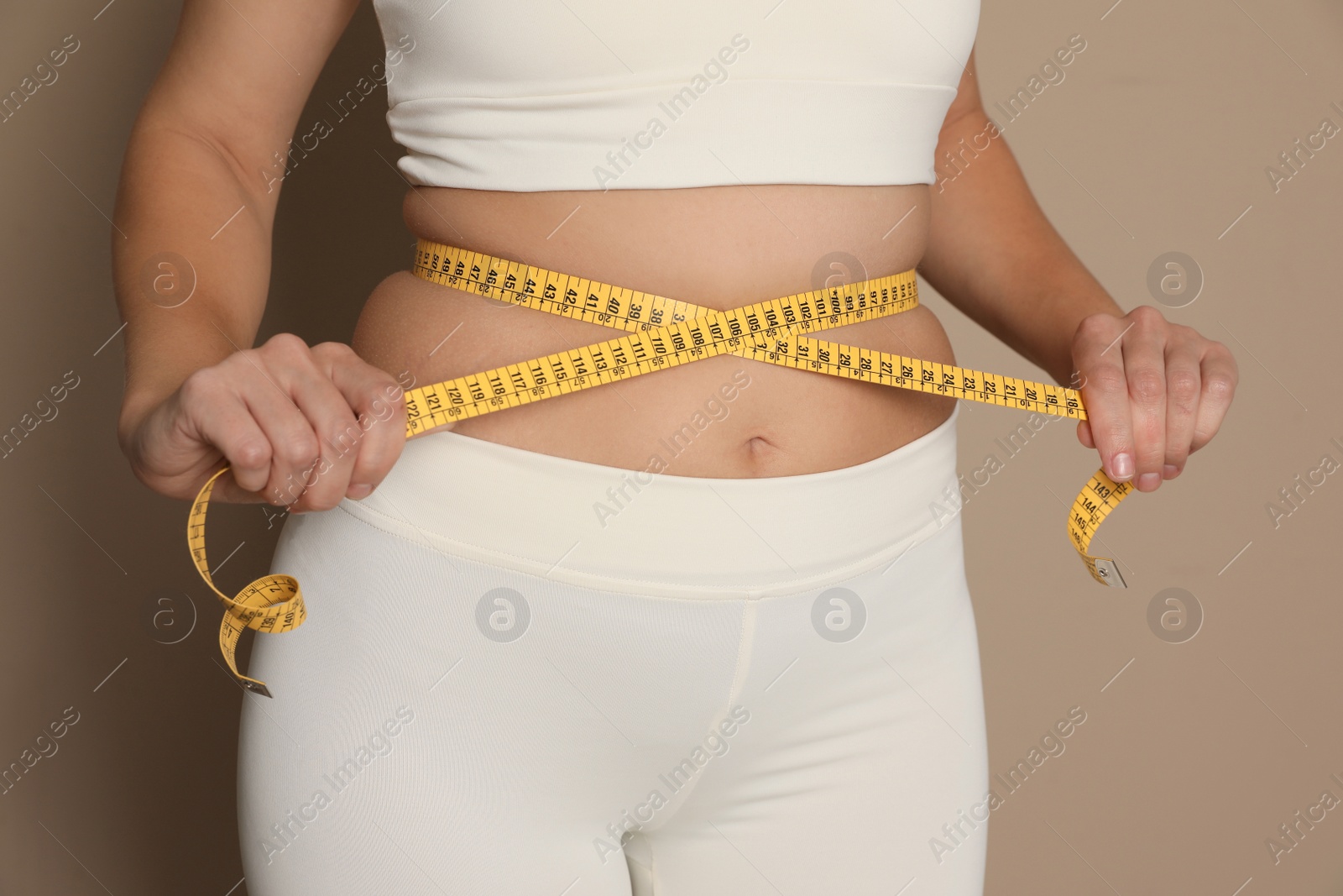 Photo of Woman measuring waist with tape on beige background, closeup