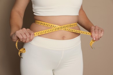 Woman measuring waist with tape on beige background, closeup