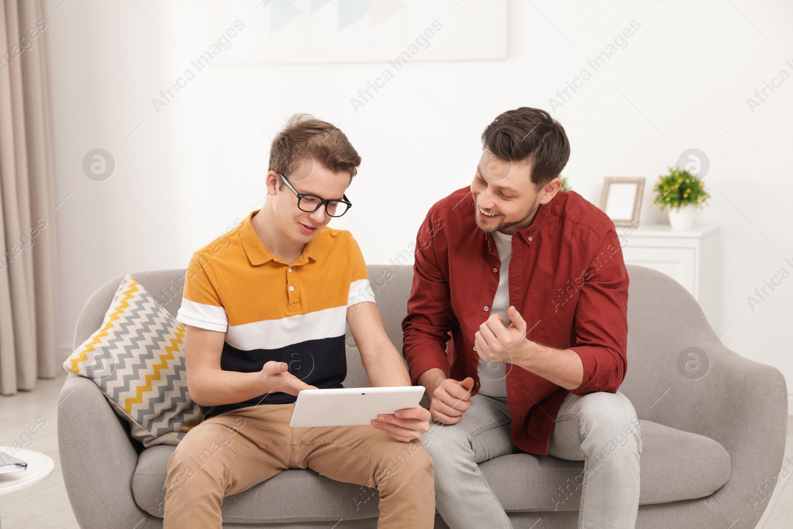 Photo of Happy father and his teenager son with tablet computer at home