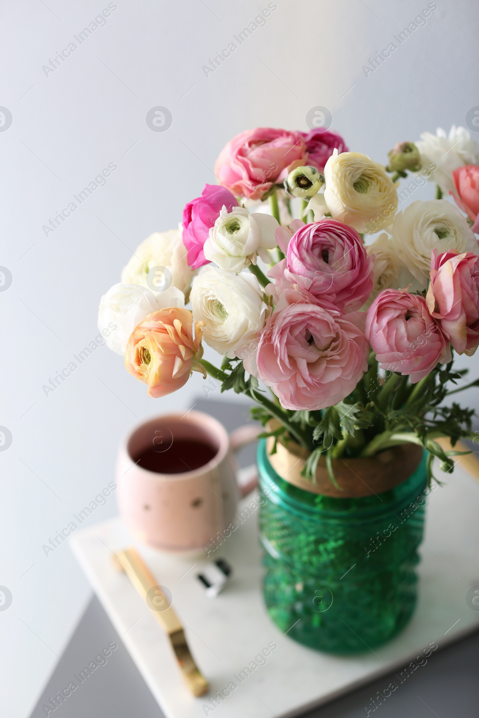 Photo of Bouquet of beautiful ranunculuses and tea on table near light grey wall