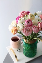 Bouquet of beautiful ranunculuses and tea on table near light grey wall