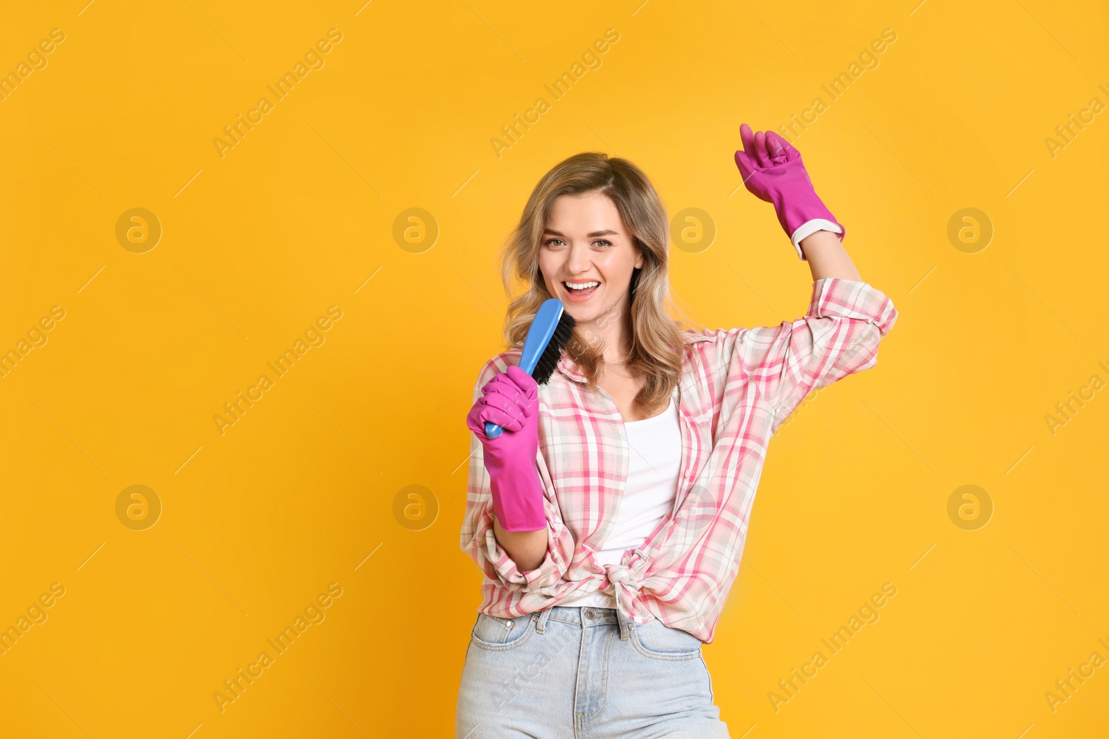 Photo of Beautiful young woman with brush singing on orange background. Space for text