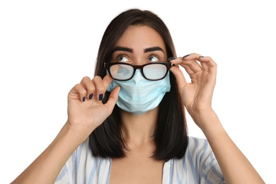Photo of Young woman wiping foggy glasses caused by wearing disposable mask on white background. Protective measure during coronavirus pandemic