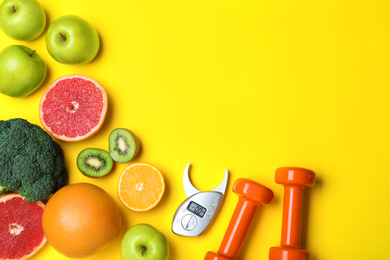 Fruits, vegetables, dumbbells and digital caliper on yellow background, flat lay with space for text. Visiting nutritionist