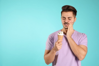 Emotional young man with sensitive teeth and ice cream on color background. Space for text