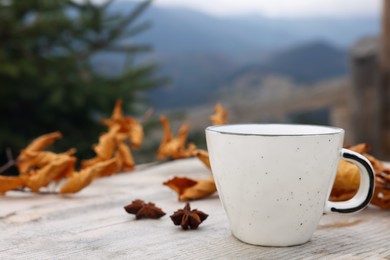 Photo of Cup of hot drink and autumn leaves on wooden table in mountains. Space for text