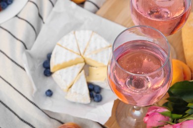 Photo of Glasses of delicious rose wine, flowers and food on white picnic blanket