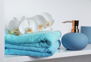 Photo of Stylish soap dispenser and towels with flowers on shelf