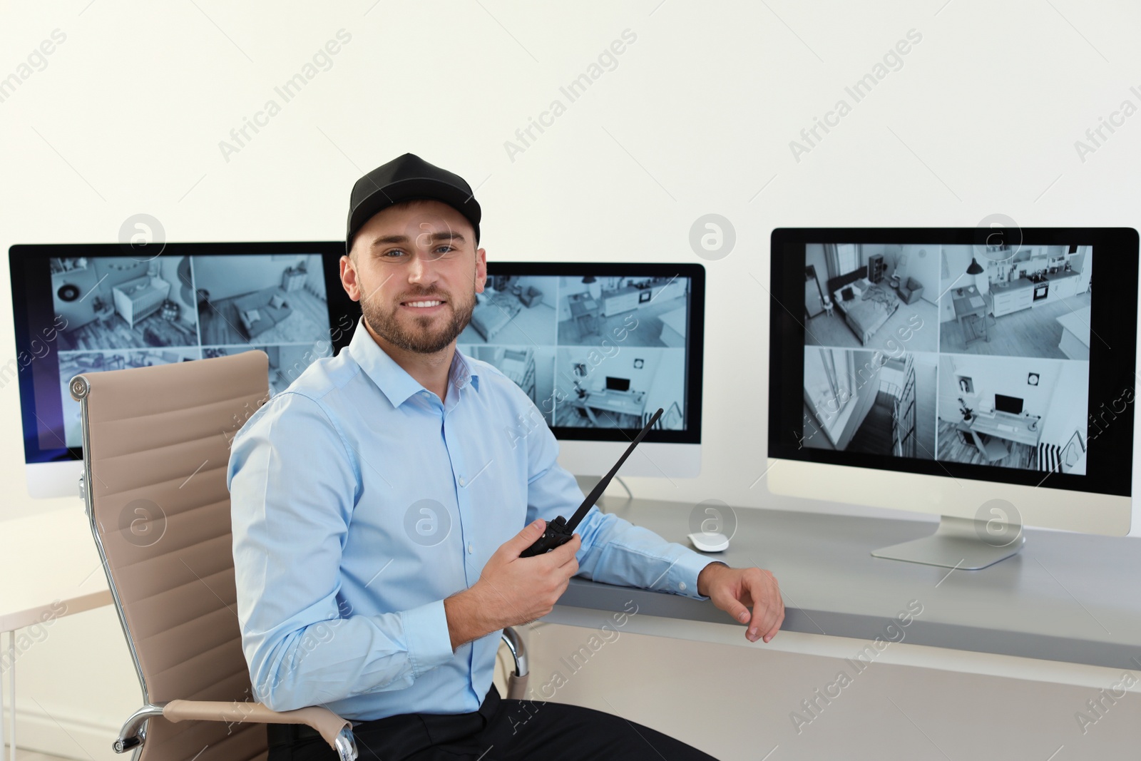 Photo of Male security guard with portable transmitter monitoring home cameras indoors