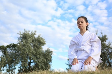 Cute little girl in kimono meditating outdoors. Karate practicing