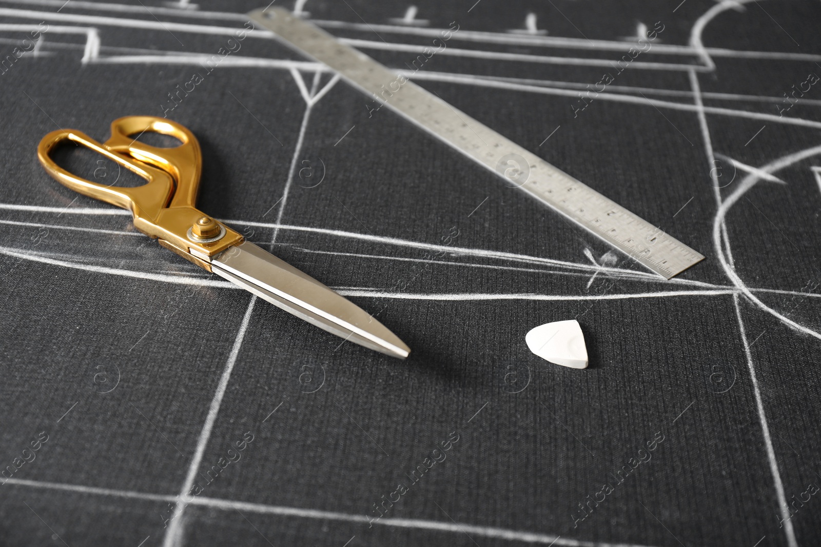 Photo of Scissors, tailor's chalk and ruler on grey fabric with sewing patterns