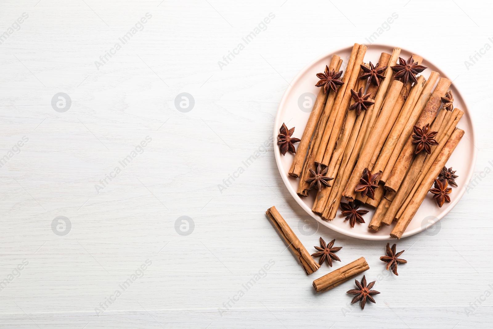 Photo of Aromatic cinnamon sticks and anise on white wooden table, flat lay. Space for text