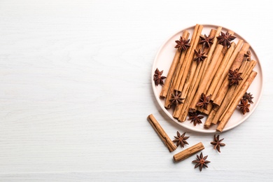 Aromatic cinnamon sticks and anise on white wooden table, flat lay. Space for text