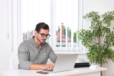 Photo of Handsome young man working with laptop at table in office