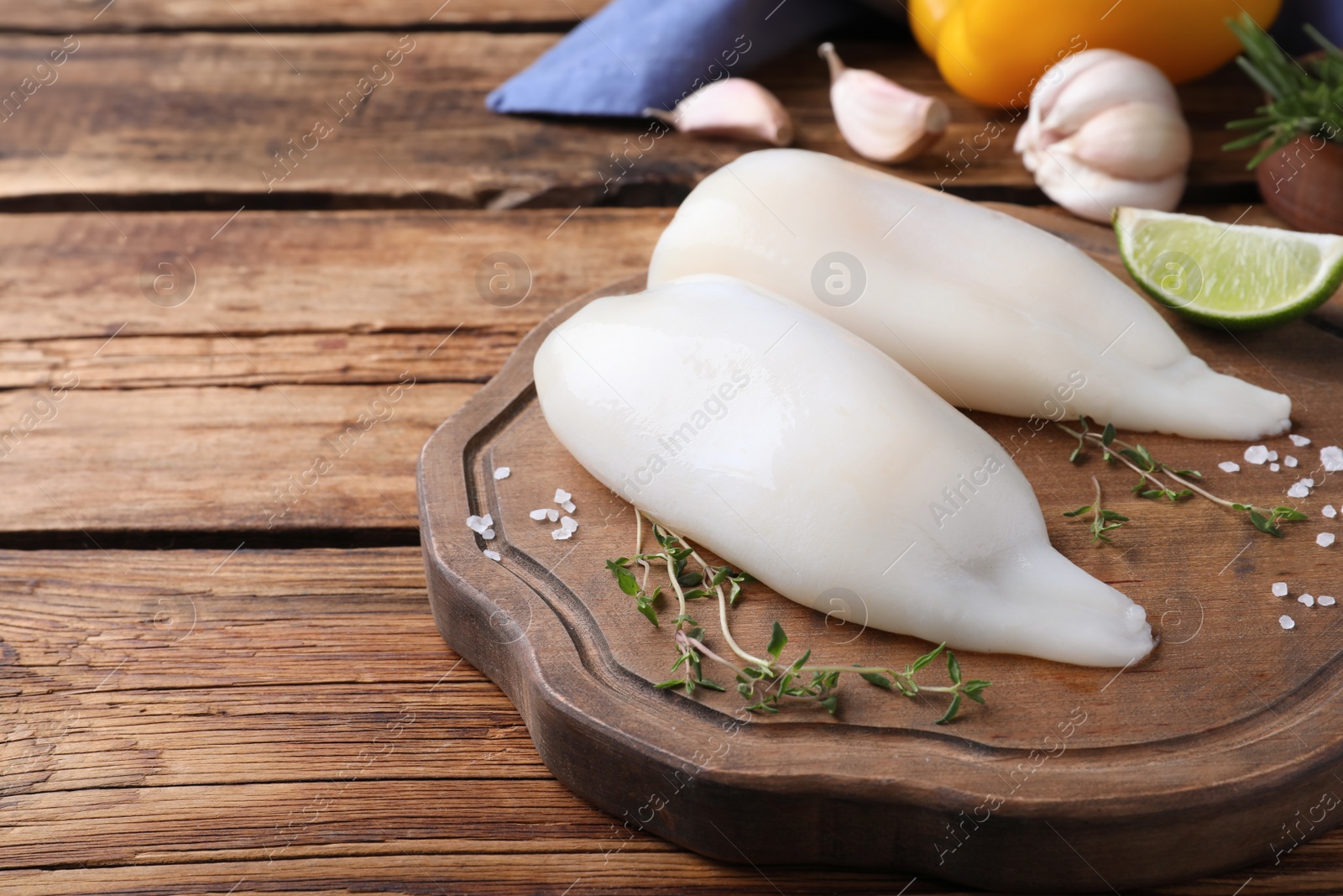 Photo of Fresh raw squid tubes with lime, thyme and salt on wooden table. Space for text