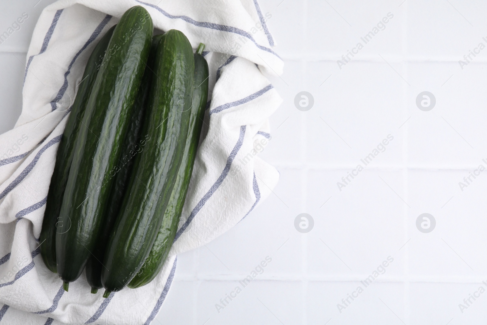 Photo of Fresh cucumbers and cloth on white tiled table, top view. Space for text