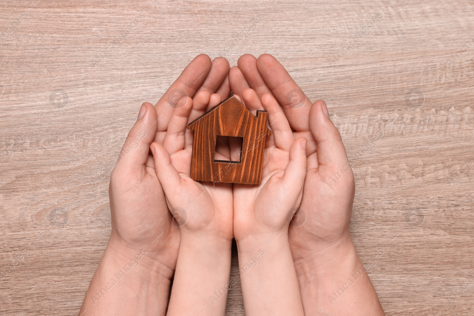 Photo of Home security concept. Man with his little child holding house model at wooden table, top view