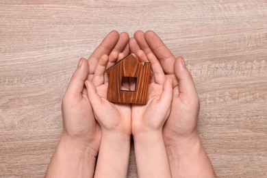 Home security concept. Man with his little child holding house model at wooden table, top view