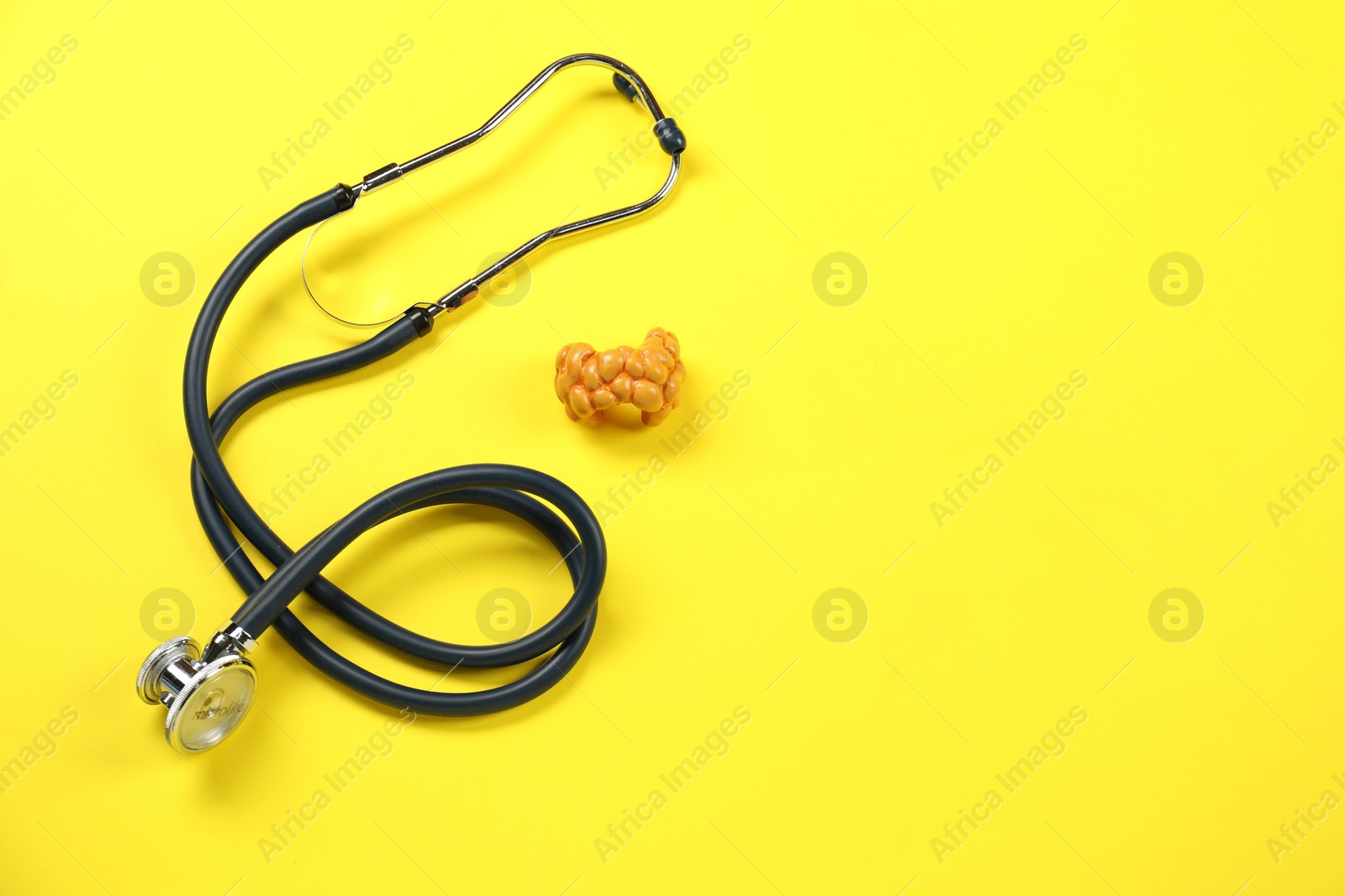 Photo of Endocrinology. Stethoscope and model of thyroid gland on yellow background, above view. Space for text