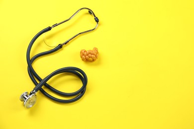 Endocrinology. Stethoscope and model of thyroid gland on yellow background, above view. Space for text