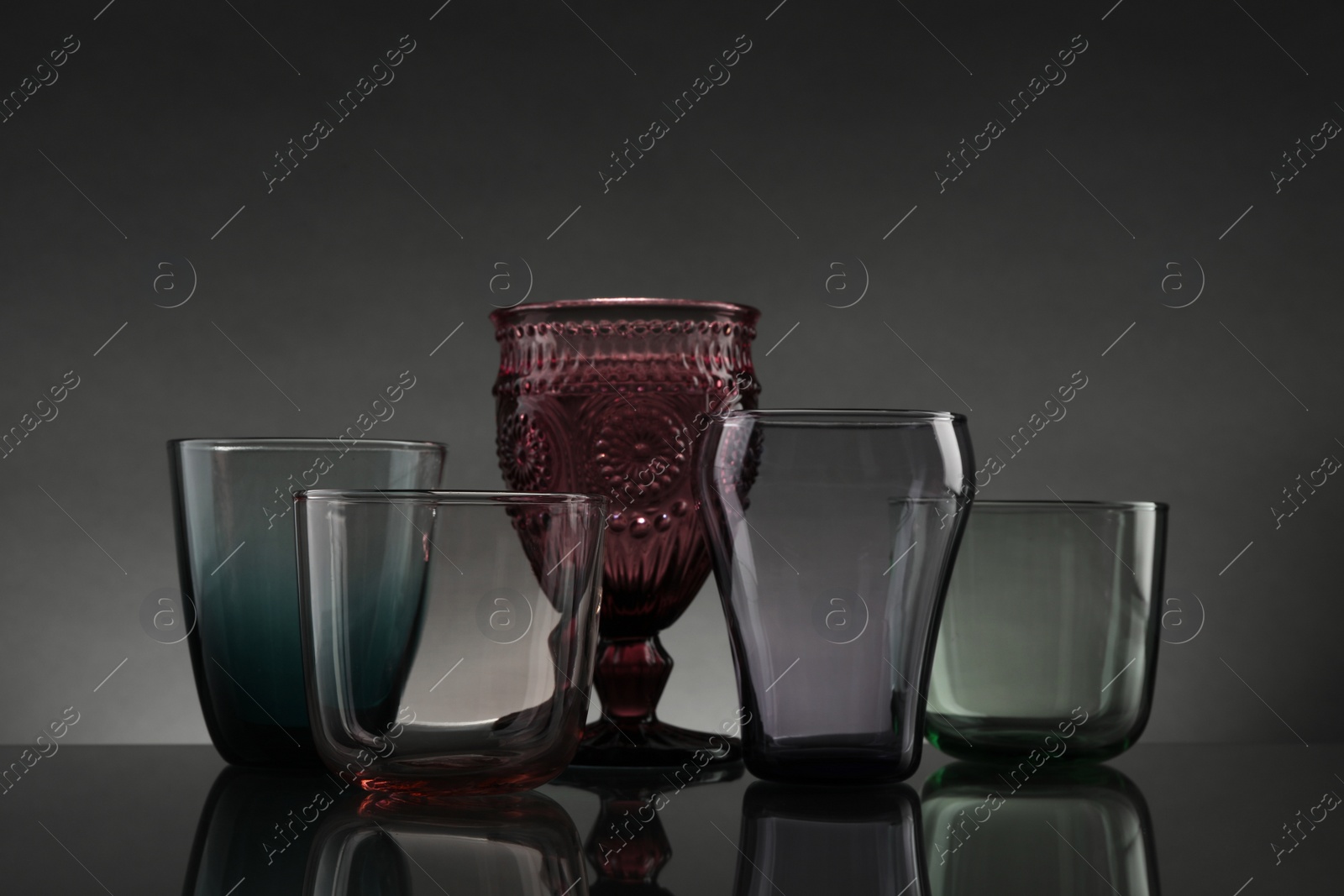 Photo of Set of different colorful empty glasses on table against grey background