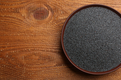 Poppy seeds in bowl on wooden table, top view. Space for text