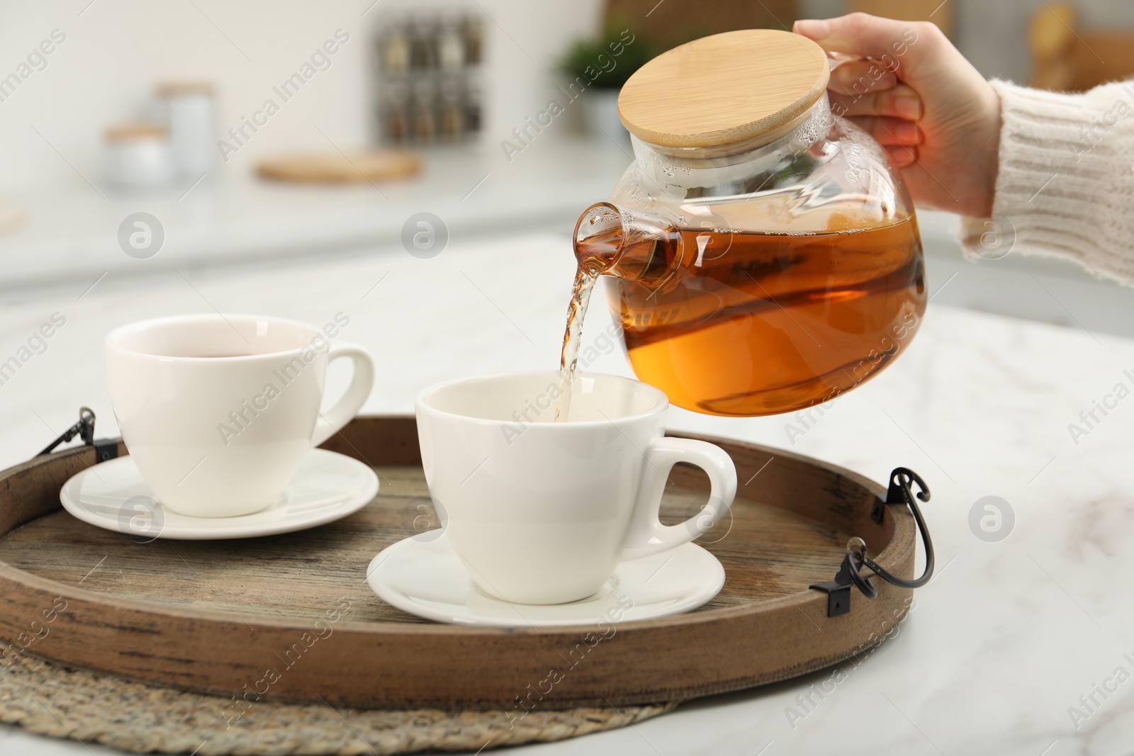 Photo of Woman pouring aromatic tea in cup at white table, closeup