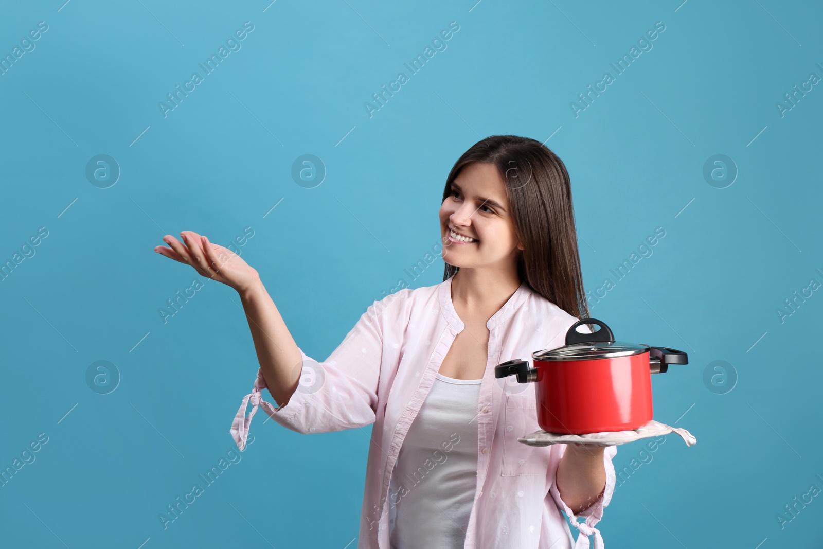 Photo of Happy young woman with cooking pot on light blue background