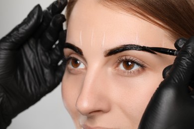 Photo of Beautician applying tint during eyebrows correction procedure on grey background, closeup