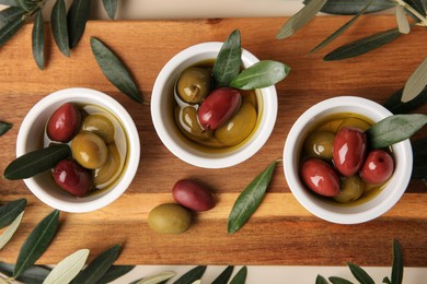 Photo of Bowls with different ripe olives and leaves on beige background, flat lay