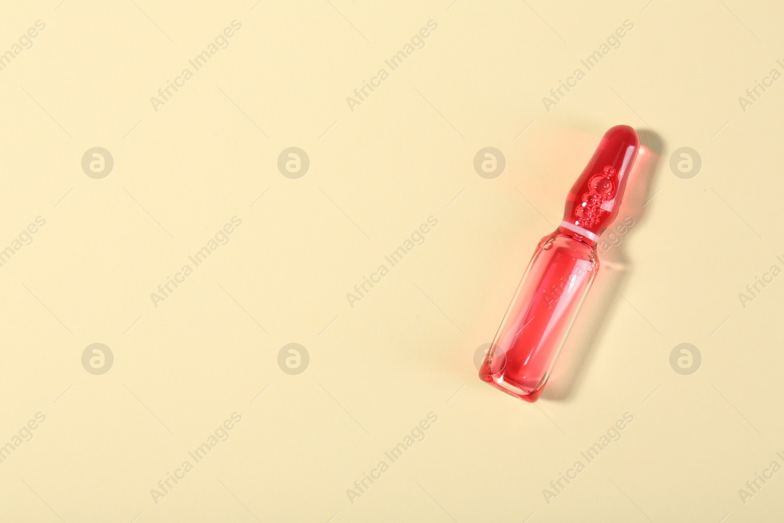 Photo of Glass ampoule with liquid on beige background, top view. Space for text