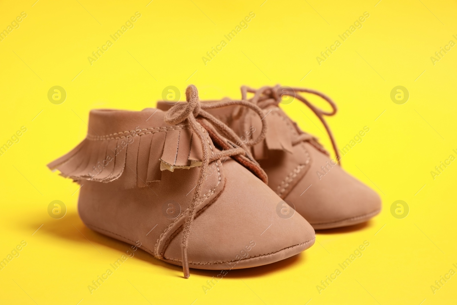 Photo of Pair of cute baby shoes on yellow background, closeup