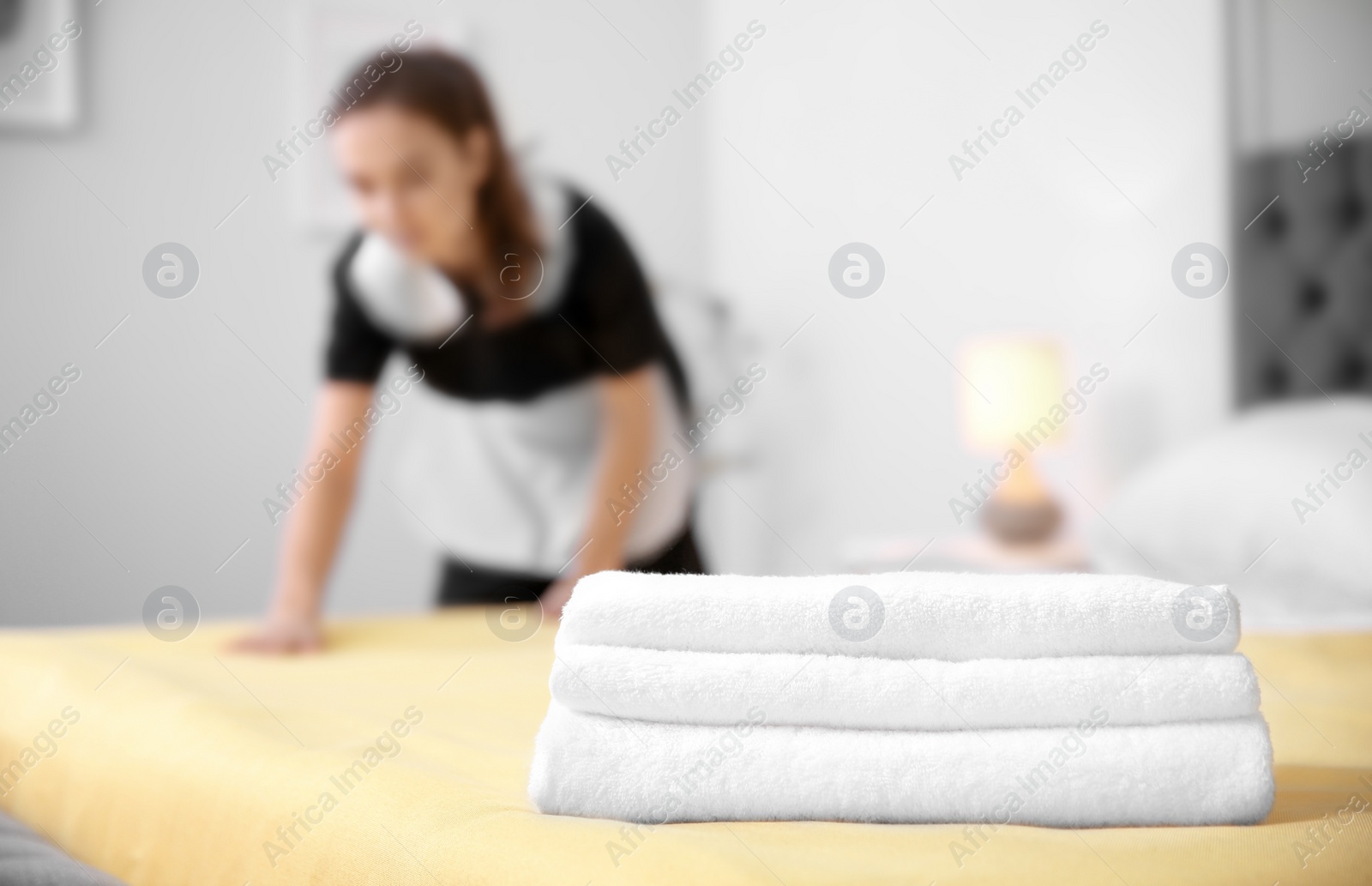 Photo of Stack of towels and blurred maid on background in hotel room