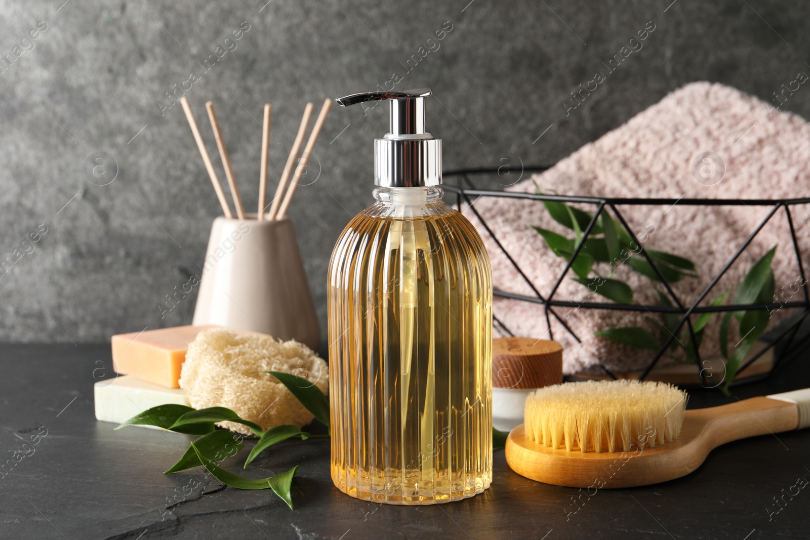 Photo of Stylish dispenser with liquid soap and other bathroom amenities on dark table