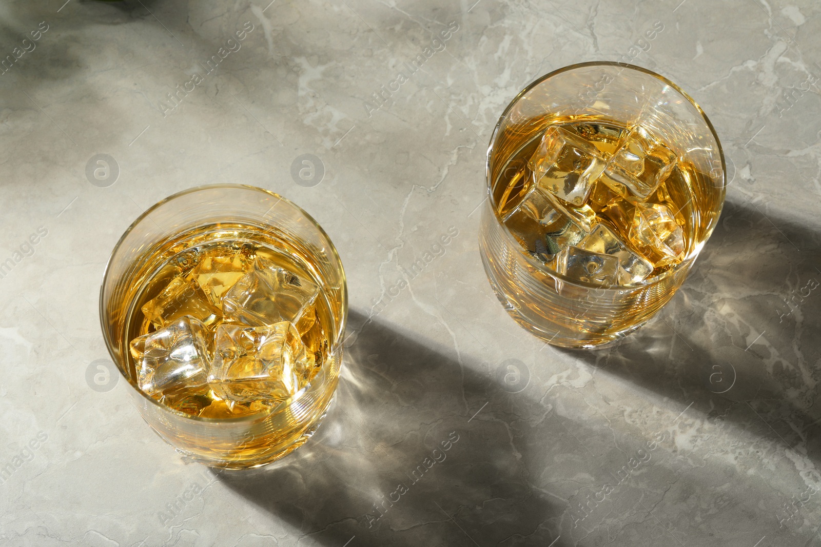 Photo of Whiskey with ice cubes in glasses on grey marble table, above view