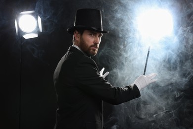 Photo of Magician wearing top hat and holding wand in smoke on stage
