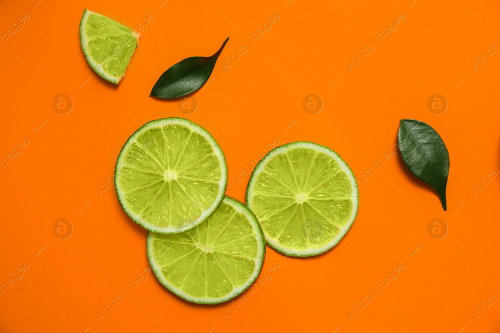 Photo of Flat lay composition with slices of fresh juicy lime on orange background