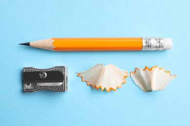Pencil, sharpener and shavings on light blue background, flat lay