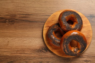 Photo of Delicious fresh bagels with poppy seeds on wooden table, top view. Space for text